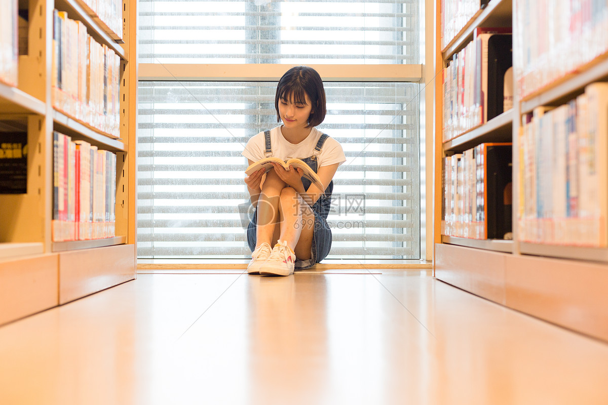 坐在图书馆书架旁看书的可爱女生