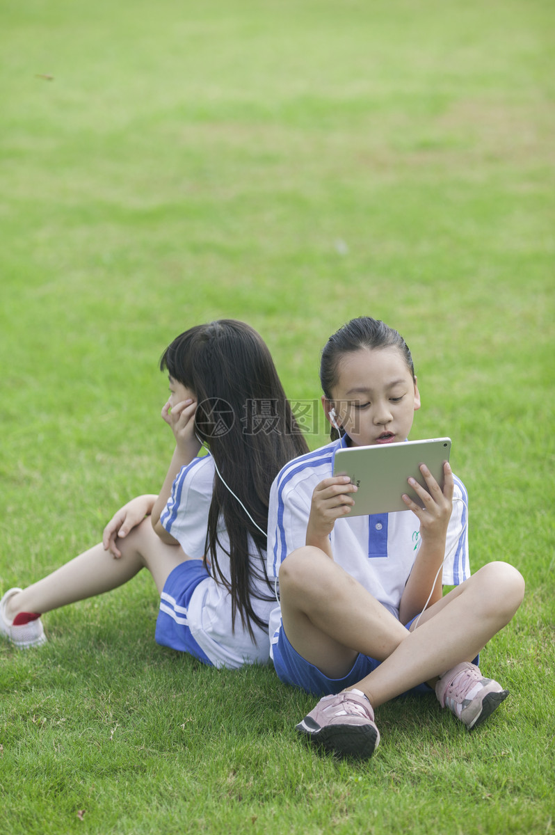 女同学在学校里草坪上用ipad学习