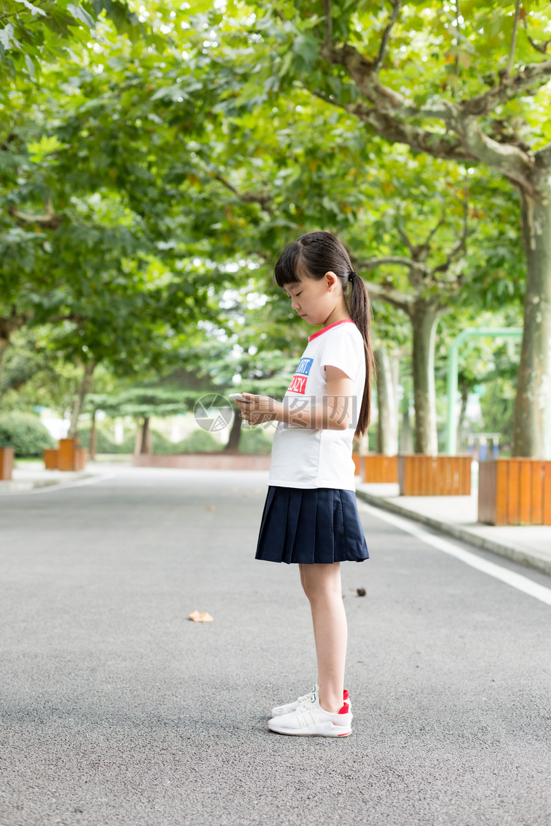 照片 教育文化 站在校园里玩手机的小学生女生.