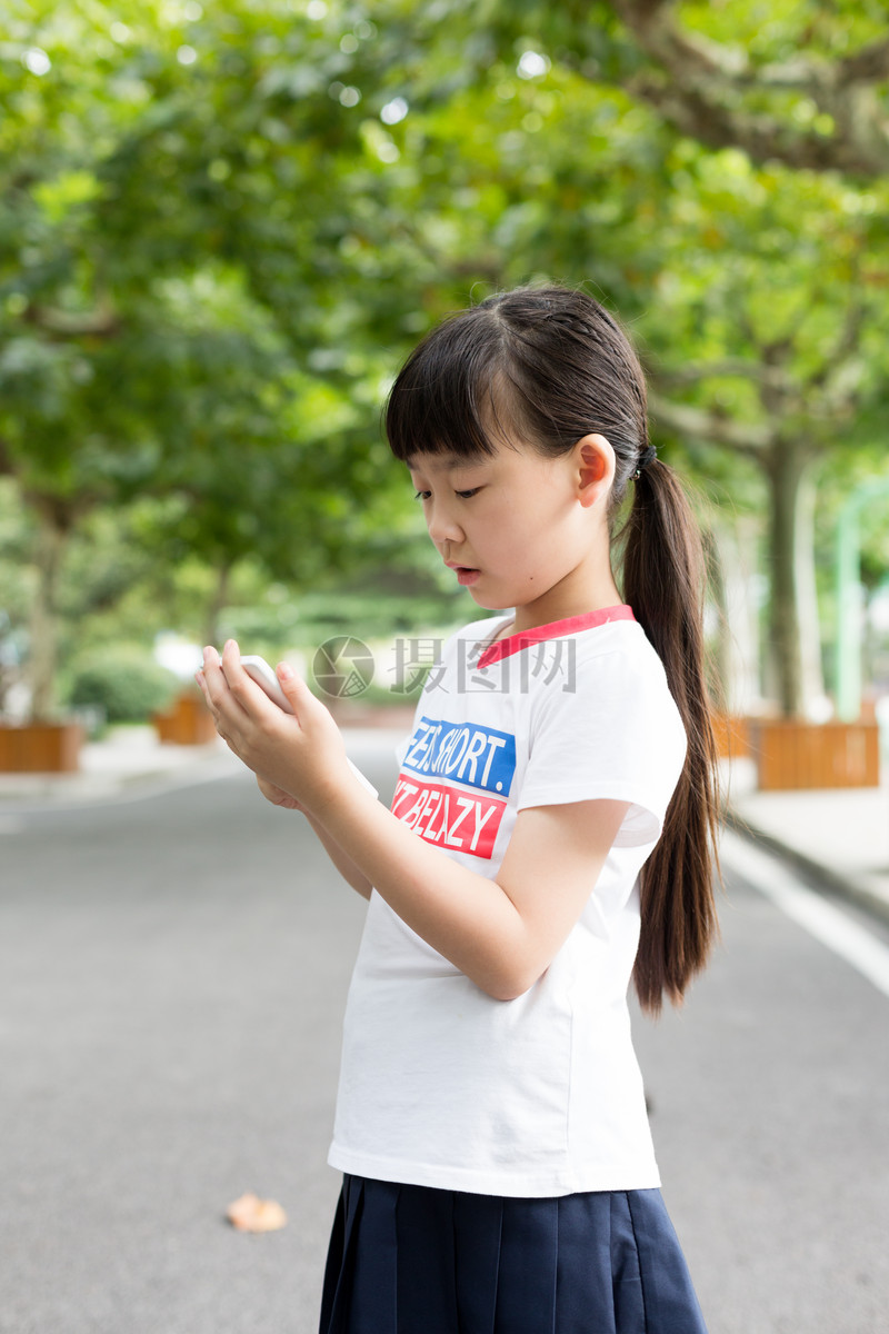 照片 教育文化 站在校园里玩手机的小学生女生.