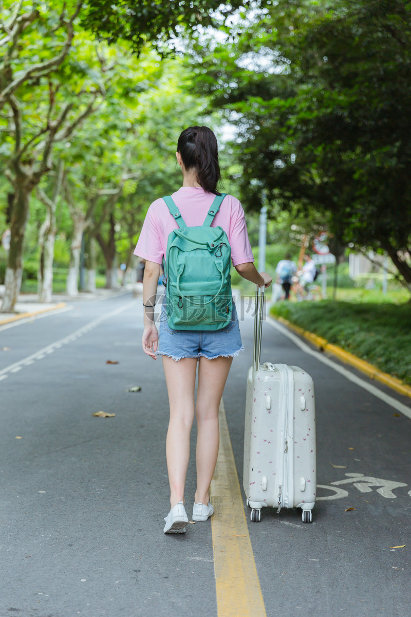 校园内女生拉旅行箱背影