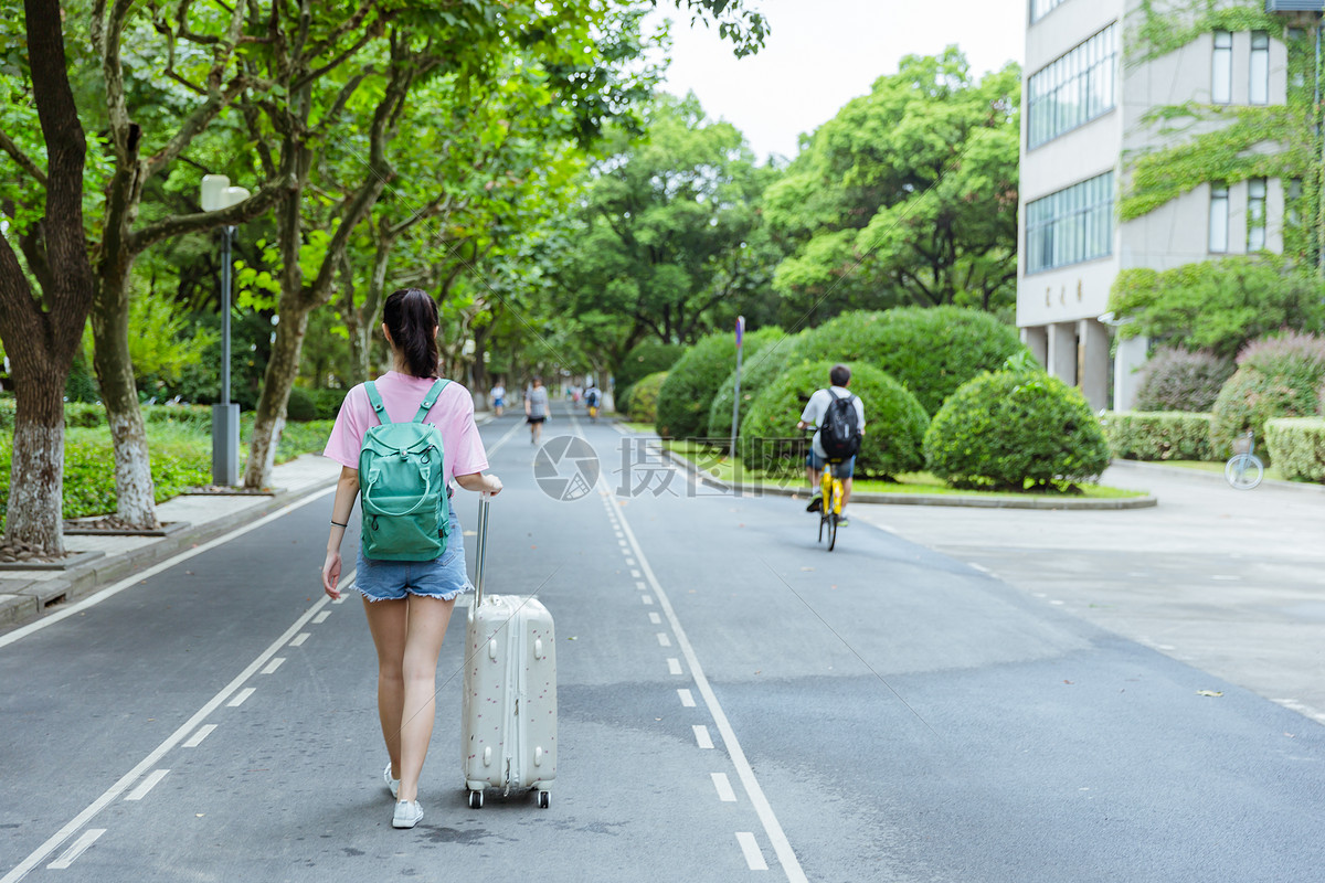 校园内女生拉旅行箱背影