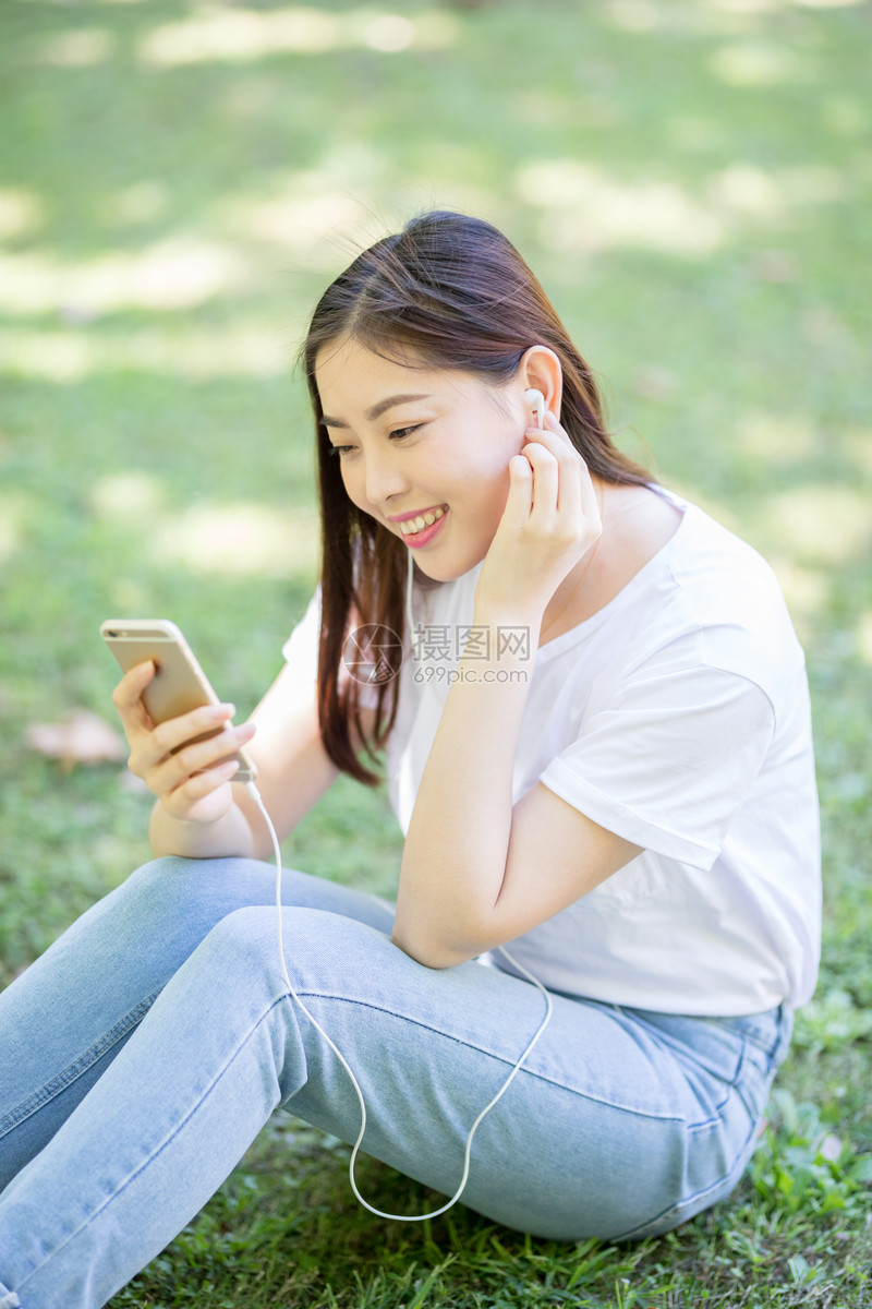 校园草坪上看手机听音乐的女生