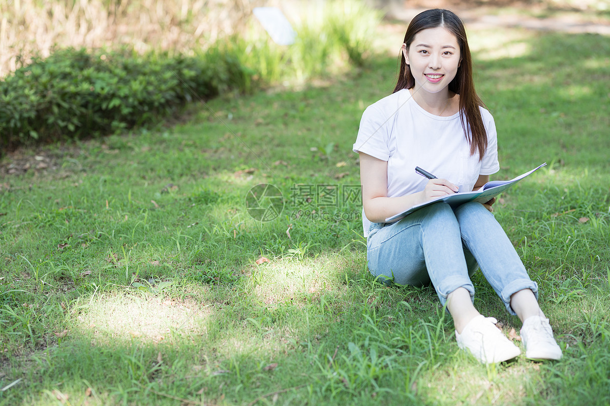 照片 人物情感 大学生 拿着课本坐在草坪上看书的大学生.