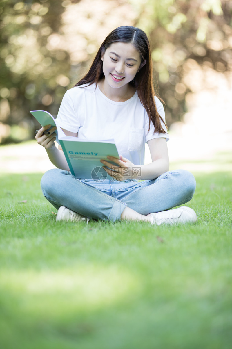 拿着课本坐在草坪上看书的大学生