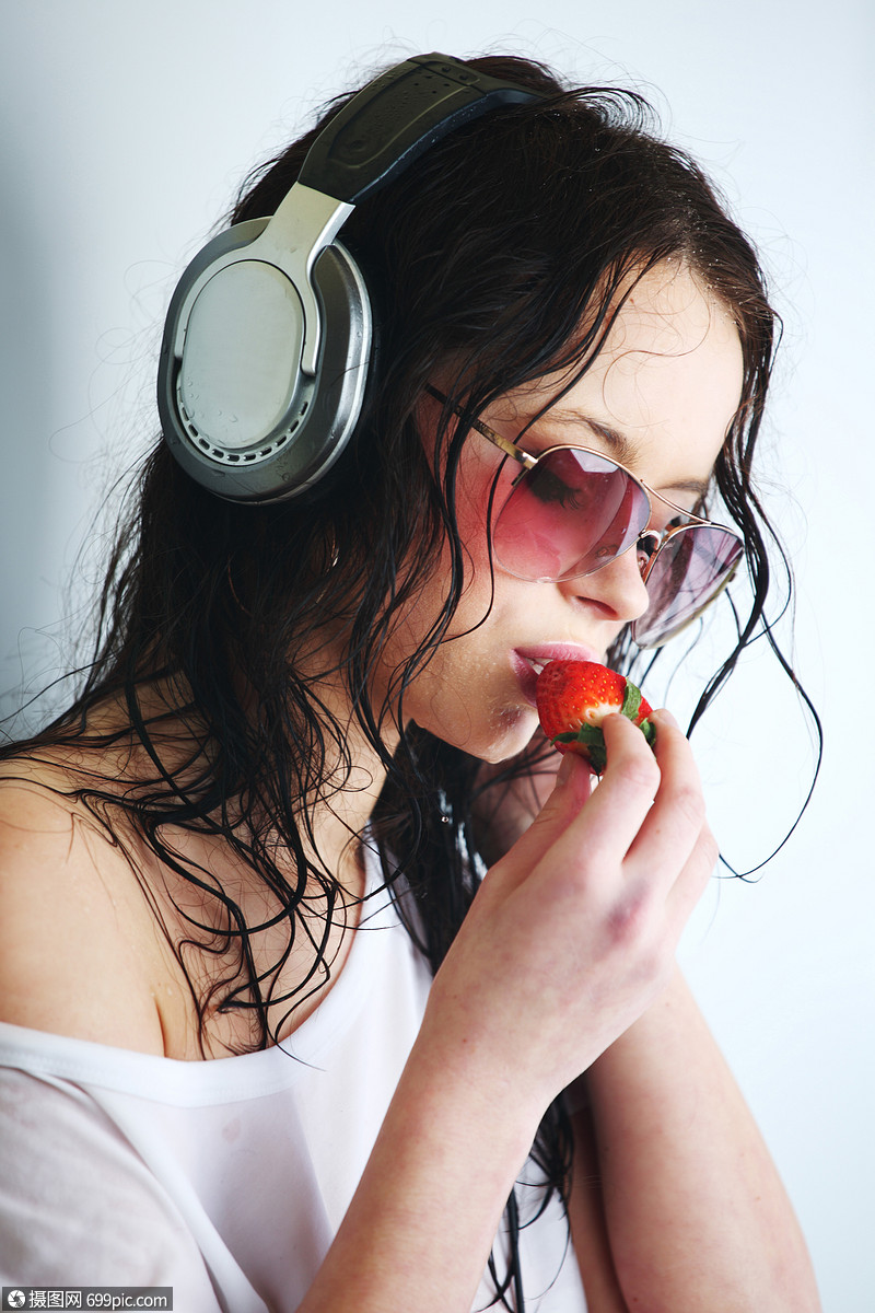的女人听耳机上的音乐草莓的光背景下女孩的特写肖像女人耳机里听音乐