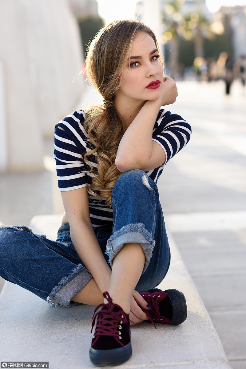 背景的长凳上漂亮的轻女孩穿着条纹t恤蓝色牛仔裤街上漂亮的俄罗斯女