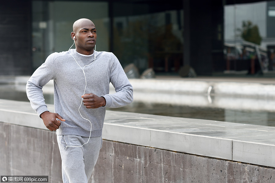 吸引力的黑人城市背景下跑步男户外锻炼用白色耳机听音乐的家伙