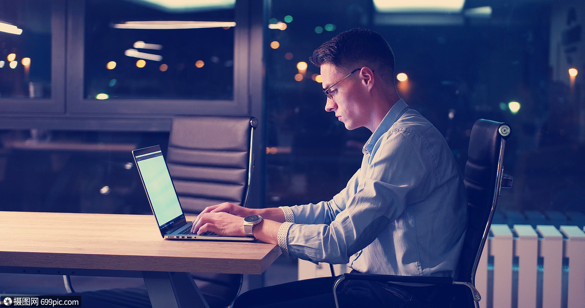 轻人晚上黑暗的办公室里用笔记本电脑工作师稍后的时间工作