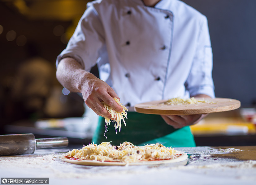 厨师把奶酪洒厨房桌子上的新鲜披萨上厨师新鲜披萨上洒奶酪包店烘烤