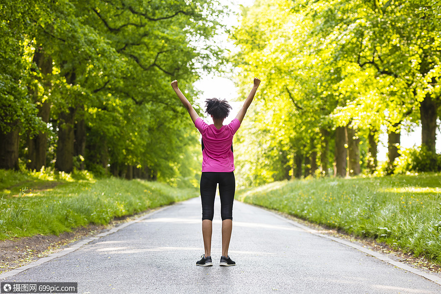 非裔美国轻女子青少健身跑步慢跑庆祝成功的道路两旁春天夏天的绿树