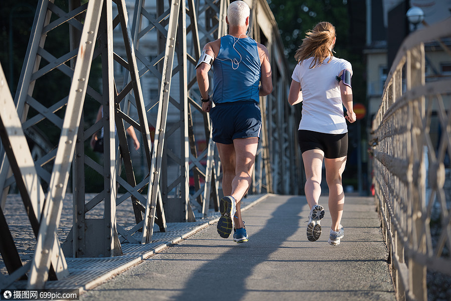 健康成熟的夫妇清晨城市慢跑,背景为日出