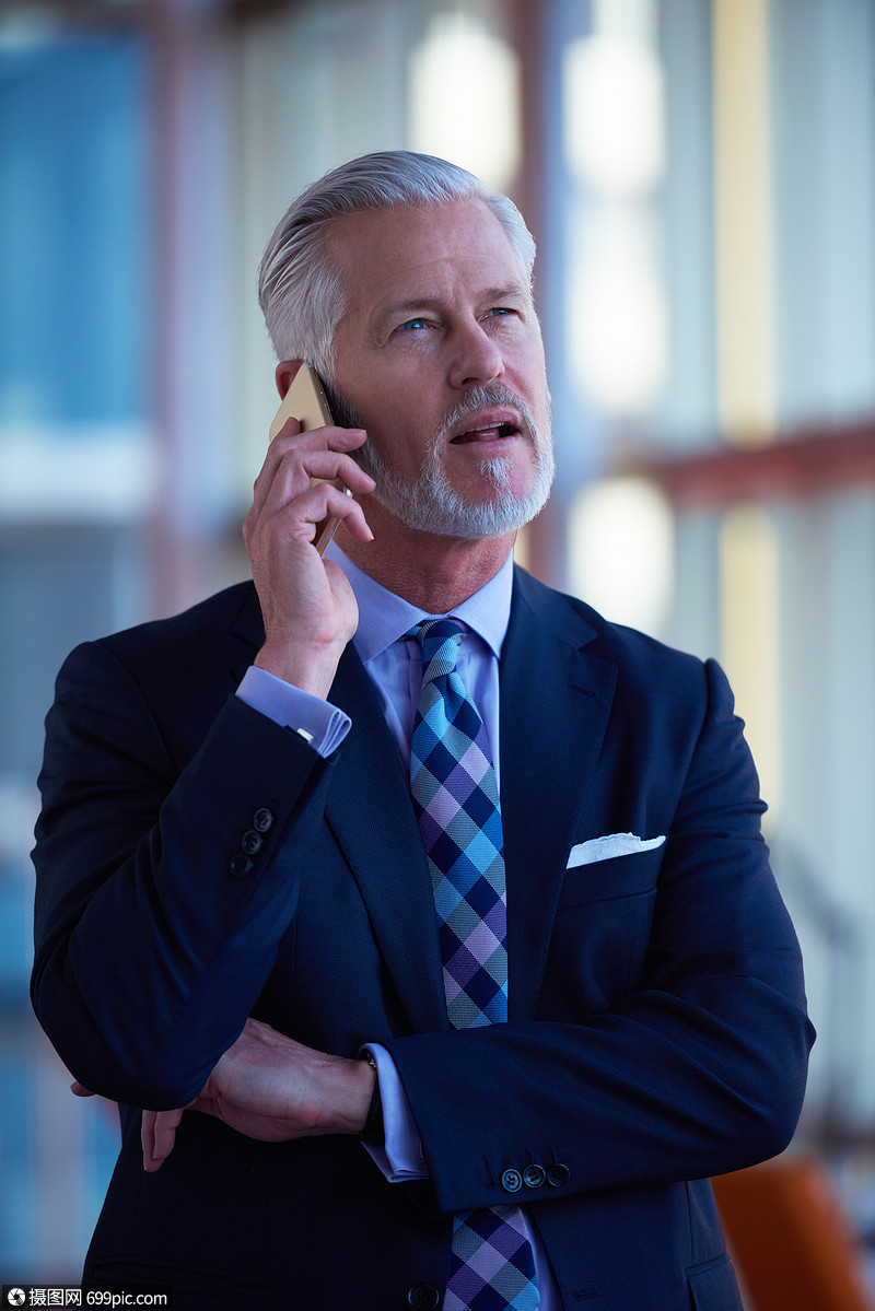 高级商务人员现代明亮的办公室内部用手机交谈