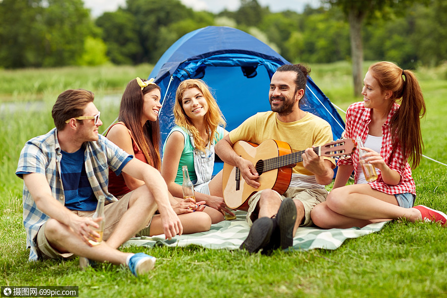 野餐人们的朋友带着帐篷饮料,露营时弹吉他