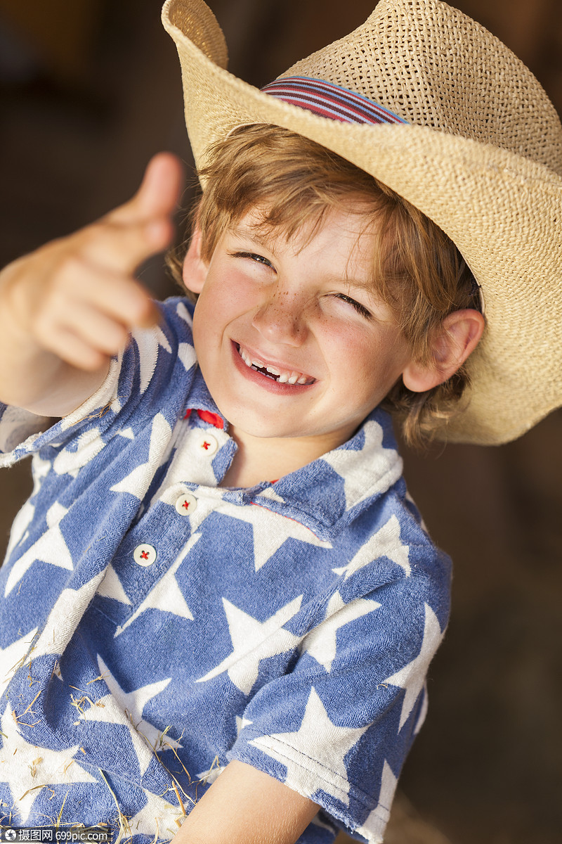 轻快乐微笑的金发男孩,穿着蓝色星星衬衫牛仔帽,坐干草干草草包上,着