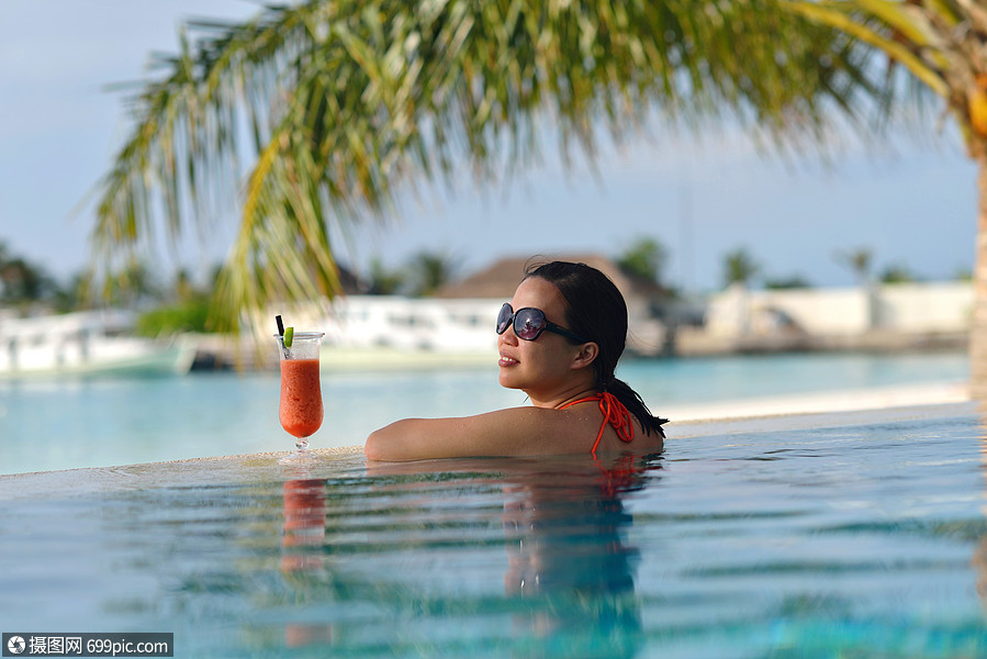 穿着比基尼的漂亮轻女人躺躺椅上,海边喝杯