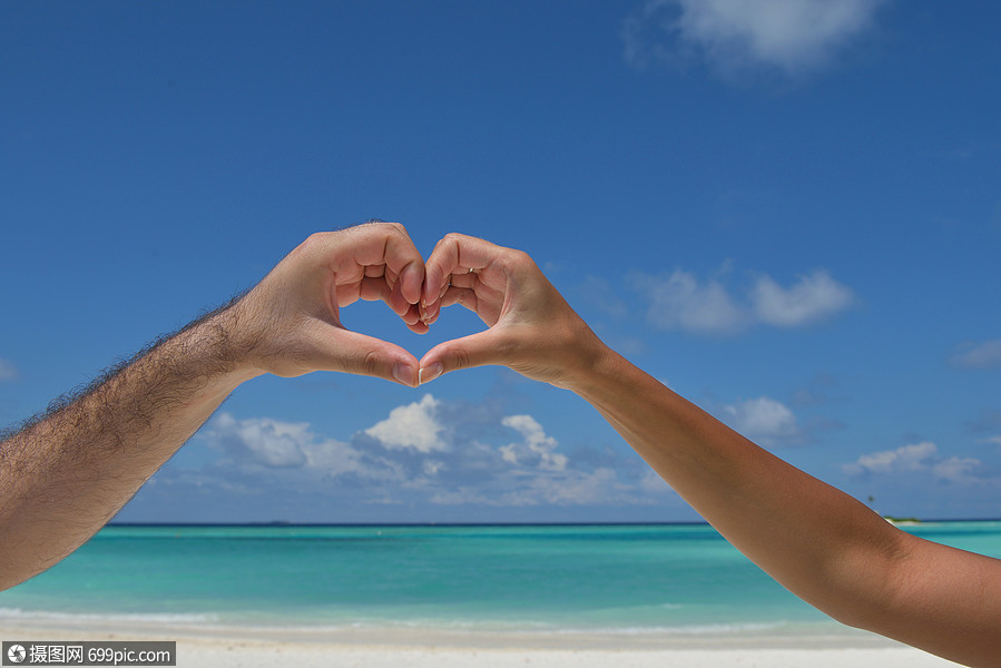 浪漫的情侣阳光明媚的热带海滩背景中的大海上用手臂制作爱情的心形