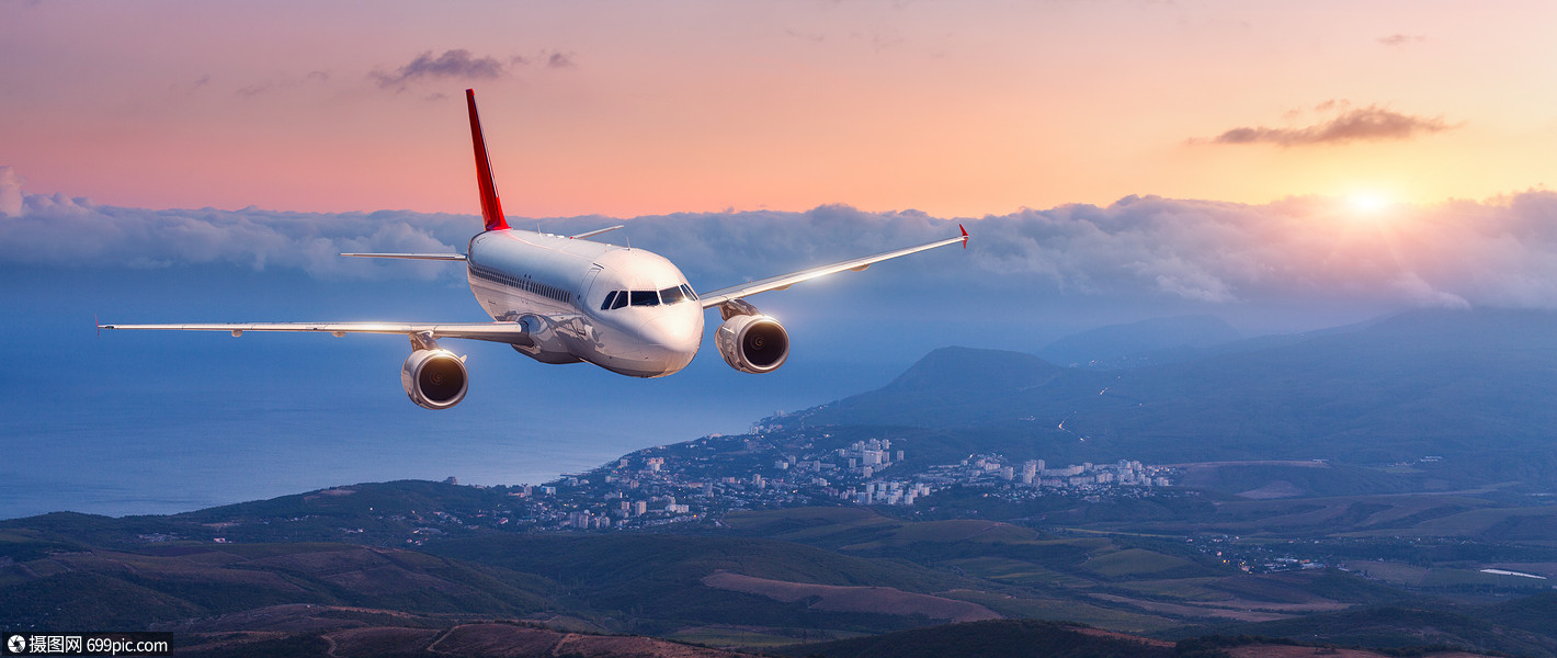 乘客飞机白色飞机的景观橙色的天空中飞行,云层覆盖着群山,大海五颜六
