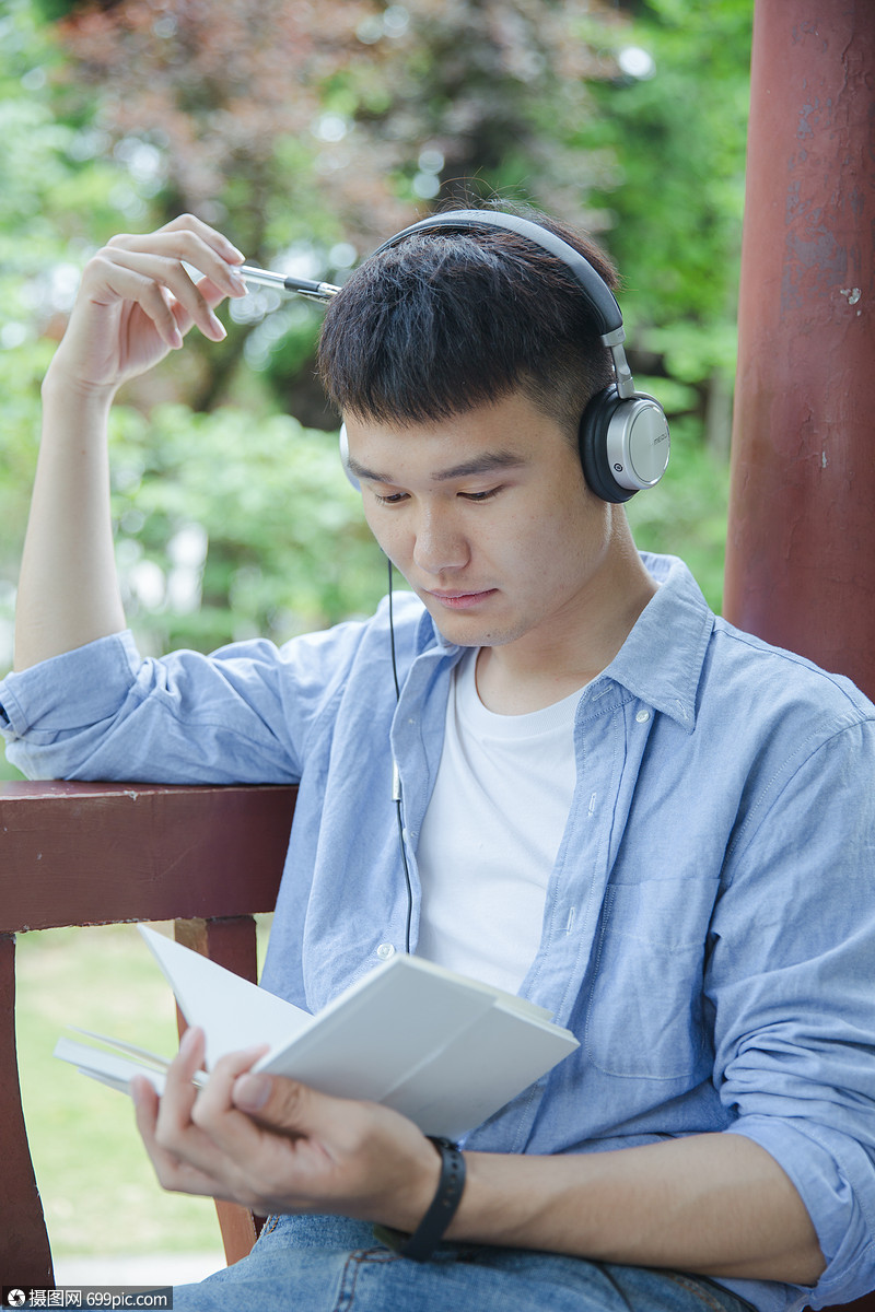 帅气大学生坐在凉亭听音乐看书