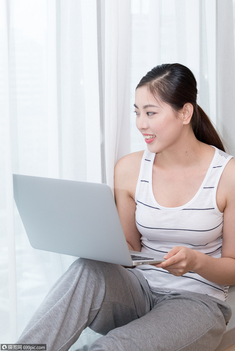 坐在客厅窗台使用笔记本电脑的美女