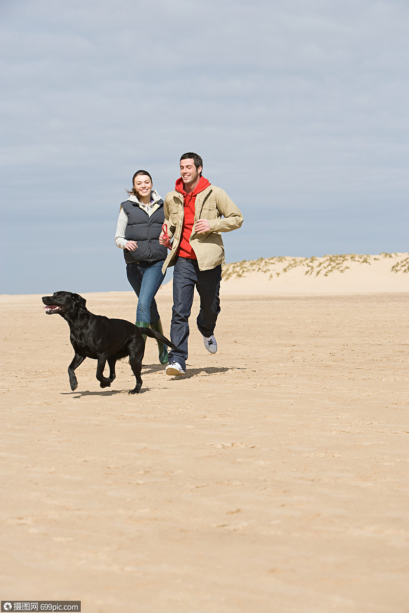 一对夫妇带着狗在海滩上奔跑
