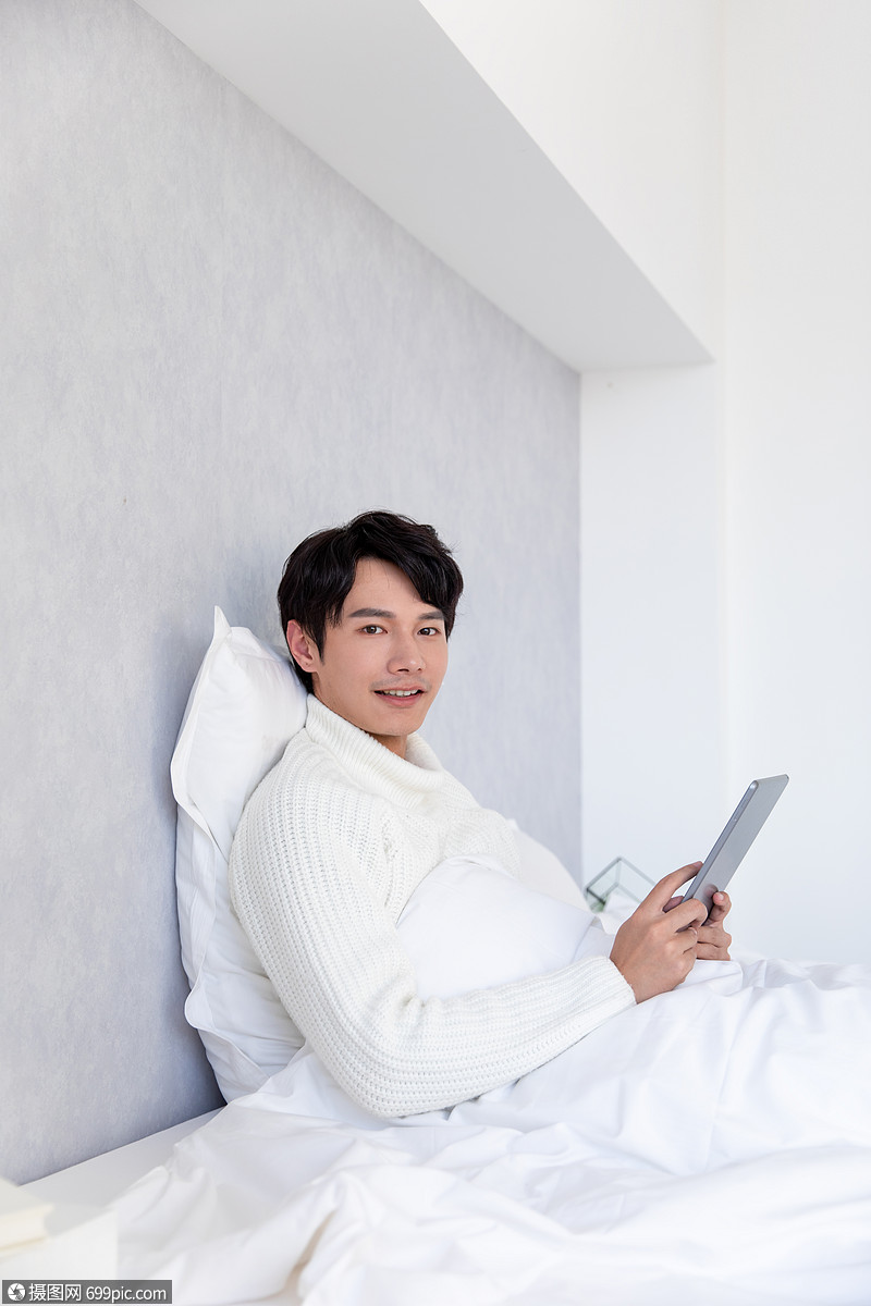 青年男性躺在床上使用平板电脑