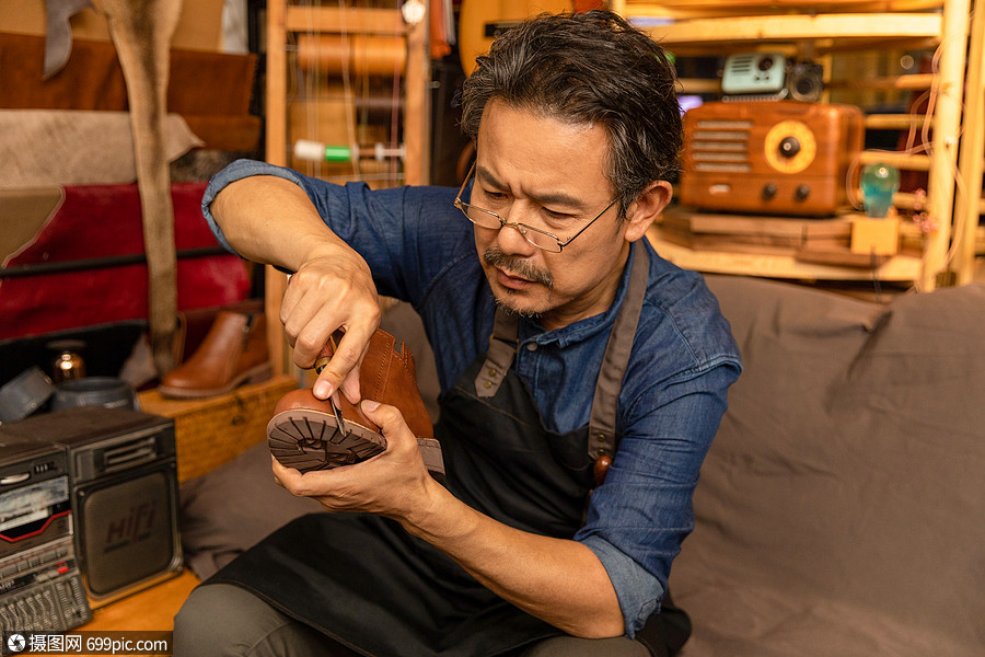 男性皮匠拿刻刀修理皮鞋工艺工具间